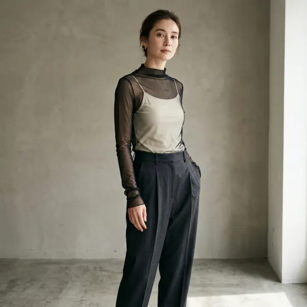 Contemporary fashion outfit combining a black sheer mesh long-sleeve top with an opaque cream camisole underneath