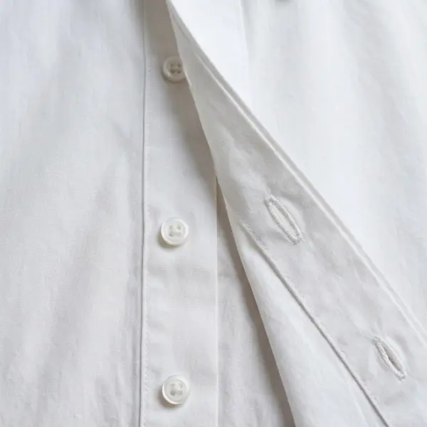 Close-up of a minimalist white shirt with a concealed button placket partially lifted to reveal the hidden buttons underneath Close-up of a minimalist white shirt with a concealed button placket partially lifted to reveal the hidden buttons underneath