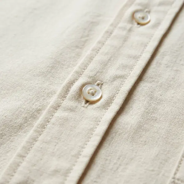 Close-up of a cotton shirt front placket showing aligned buttons, buttonholes, folded fabric layers, and precise topstitching